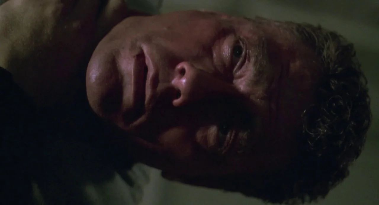 Universal Soldier: The Return (1999) movie still: closeup — A dimly lit indoor space with the man positioned close to the lens. The man lies on his…