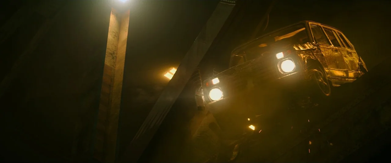 Black Widow (2021) movie still: wide — An aged SUV is perched precariously on a dark, heavy industrial concrete bridge structure. The vehicle's…