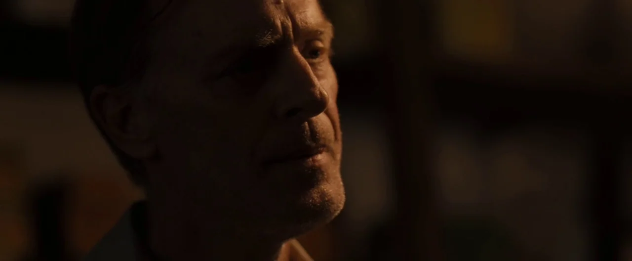 Ain’t Them Bodies Saints (2013) movie still: closeup — A dimly lit indoor space with heavy shadows obscuring the background. An older man with light…