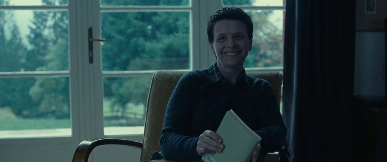 Clouds of Sils Maria (2014) movie still: medium — A quiet residential room features a large window overlooking a blurred green garden. A woman sits…
