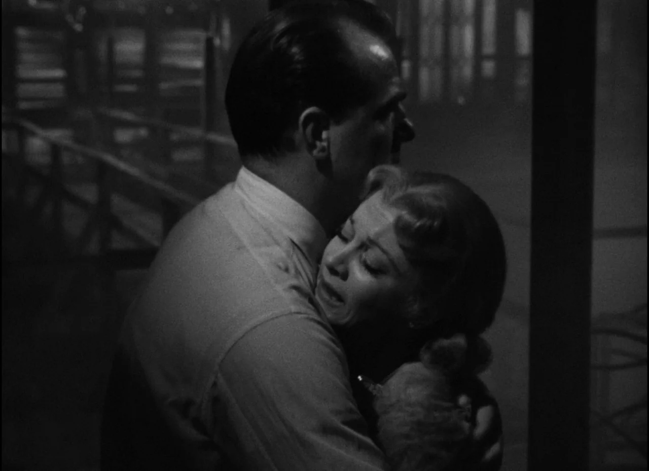 A Streetcar Named Desire (1951) movie still: medium — A dark wooden pier at night with fog hanging over the water. A man and a woman are standing…