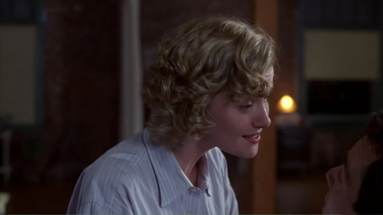 Music from Another Room (1998) movie still: medium — A dimly lit indoor space with brick walls and blurred background features. A blonde woman with…