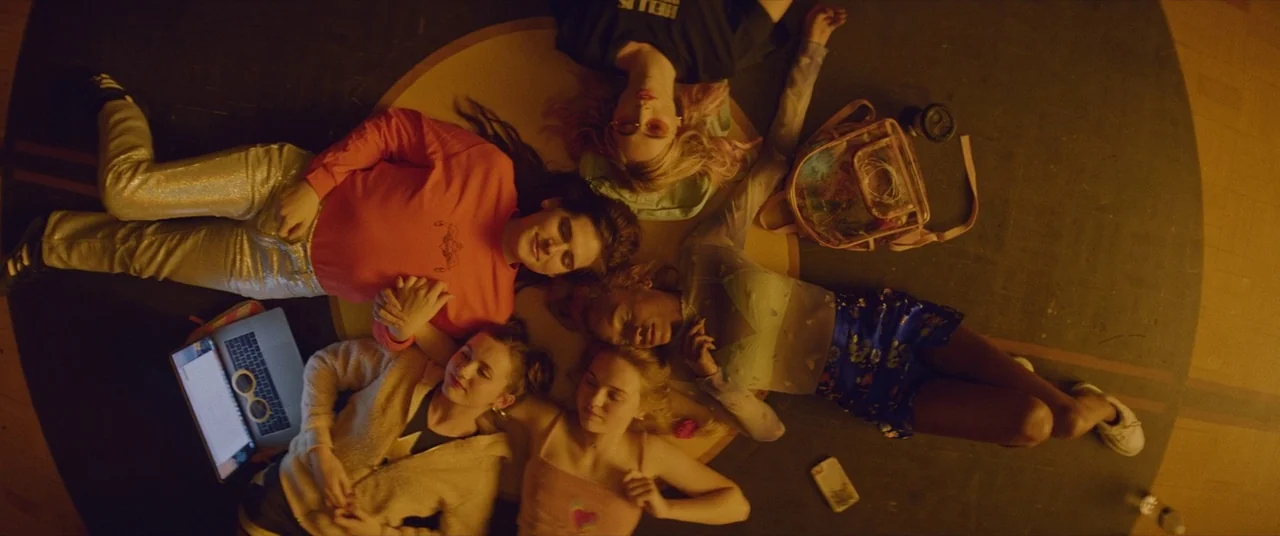 Assassination Nation (2018) movie still: wide — A high-angle shot captures five young women lying in a star pattern on floorboards. They rest their…