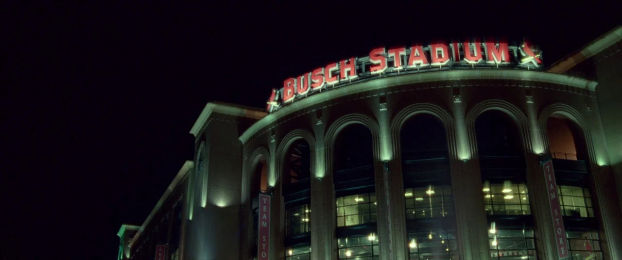 Mississippi Grind (2015) movie still: establishing — The exterior of a baseball stadium at night with arched windows and stone masonry. A large…