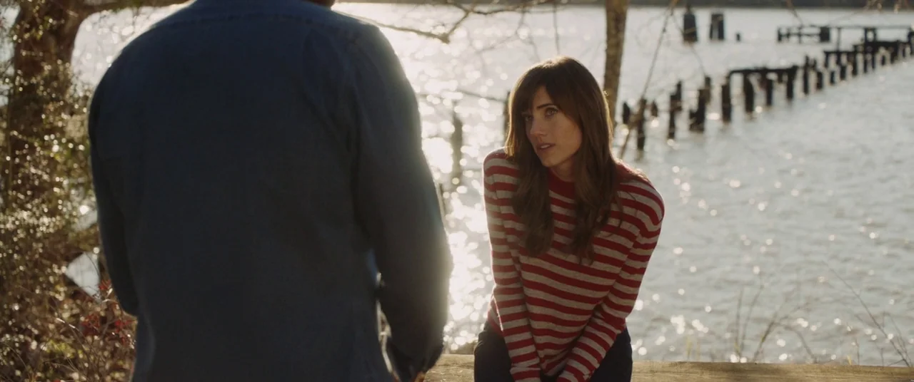 Get Out (2017) movie still: medium — A wooden pier extends over a bright, reflective body of water at daytime. A man stands in the foreground facing…
