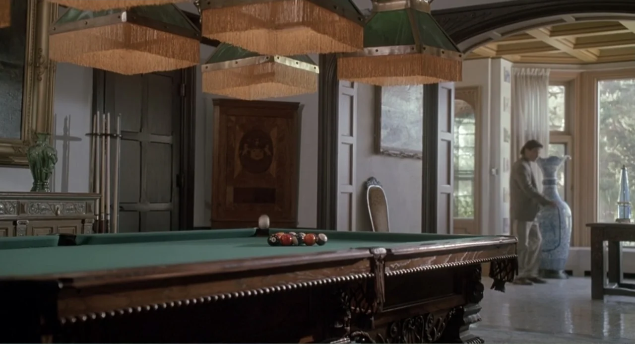 F/X2 (1991) movie still: medium — A spacious room features a large pool table under multiple low-hanging green shaded lamps. A man stands in the…