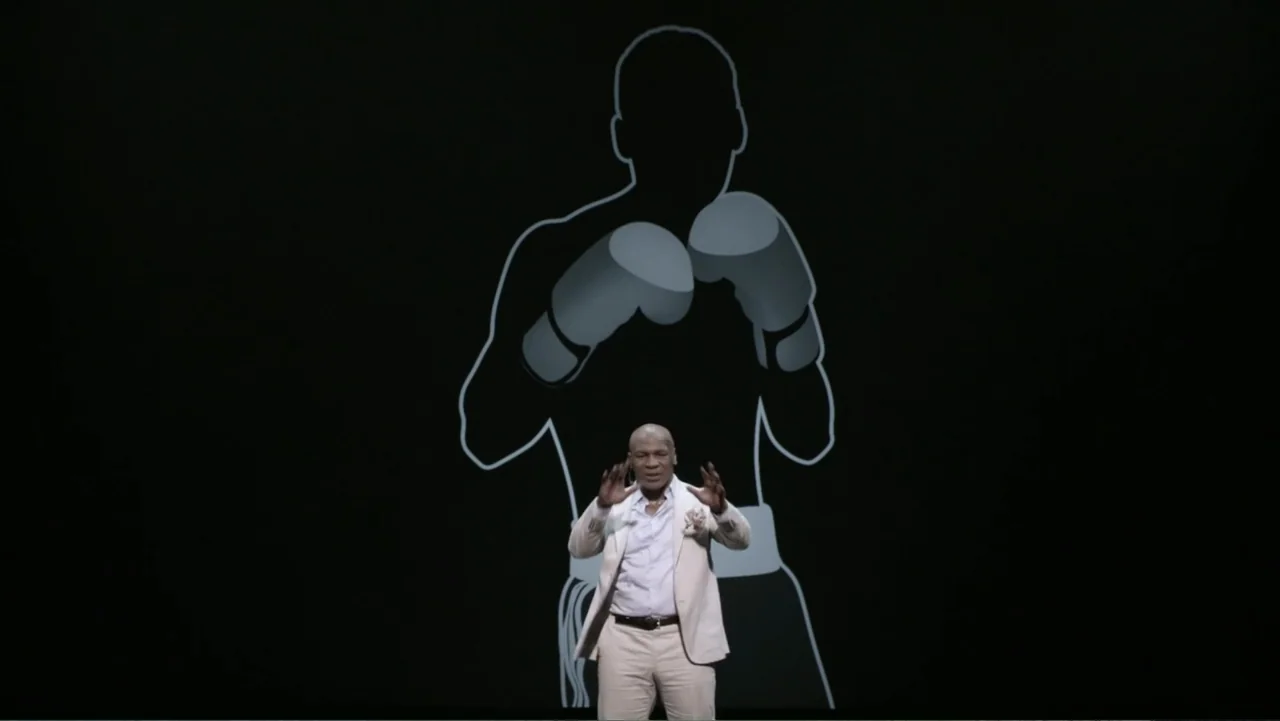 Mike Tyson: Undisputed Truth (2013) movie still: medium — A man stands on a dark stage with a large white outline projection. The man gestures with…