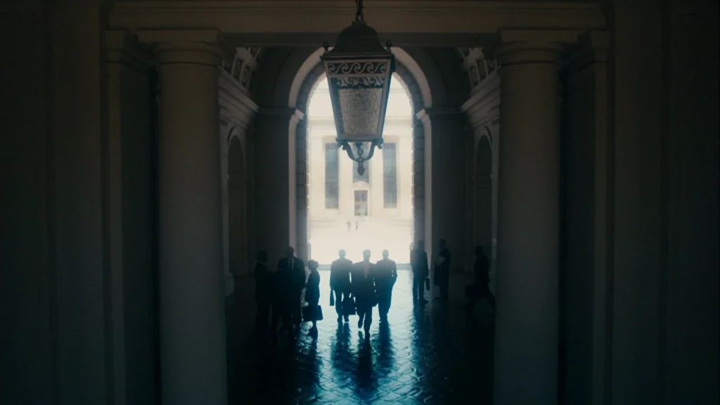The Informant! (2009) movie still: wide — A stone corridor with tall columns is illuminated by light streaming through an archway. Silhouetted…