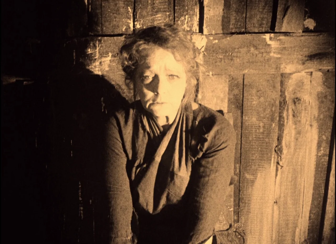 The Phantom Carriage (1921) movie still: medium — A woman stands before a wall of rough, vertically-laid wooden planks. The woman is centered in the…