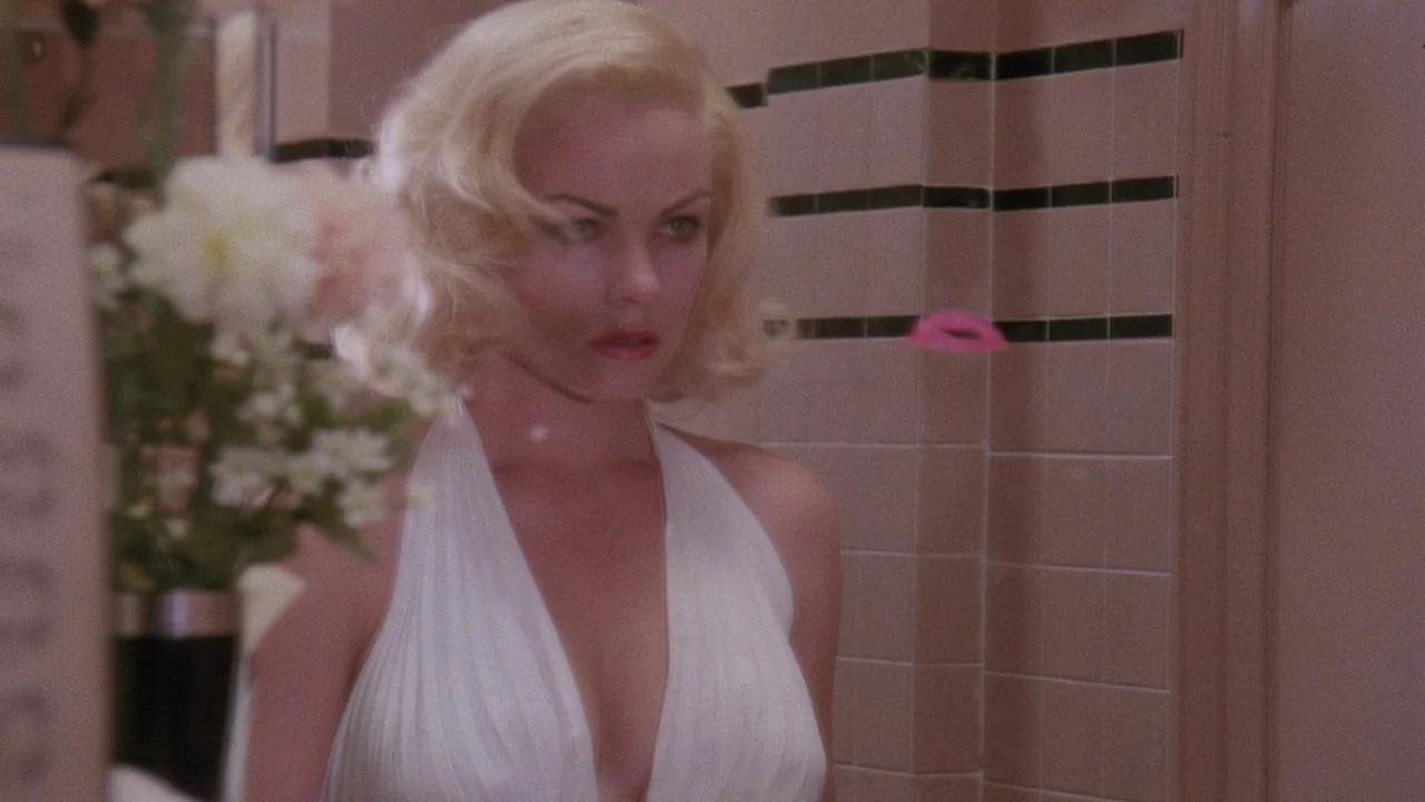 Insignificance (1985) movie still: medium — A vintage tiled bathroom features horizontal black accents along the wall tiles. A blonde woman in a…