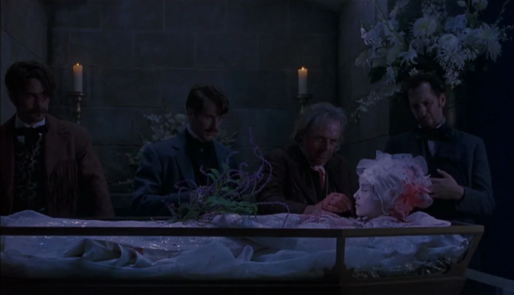 Bram Stoker’s Dracula (1992) movie still: wide — A stone-walled crypt contains a glass-topped coffin surrounded by floral arrangements and candles.…