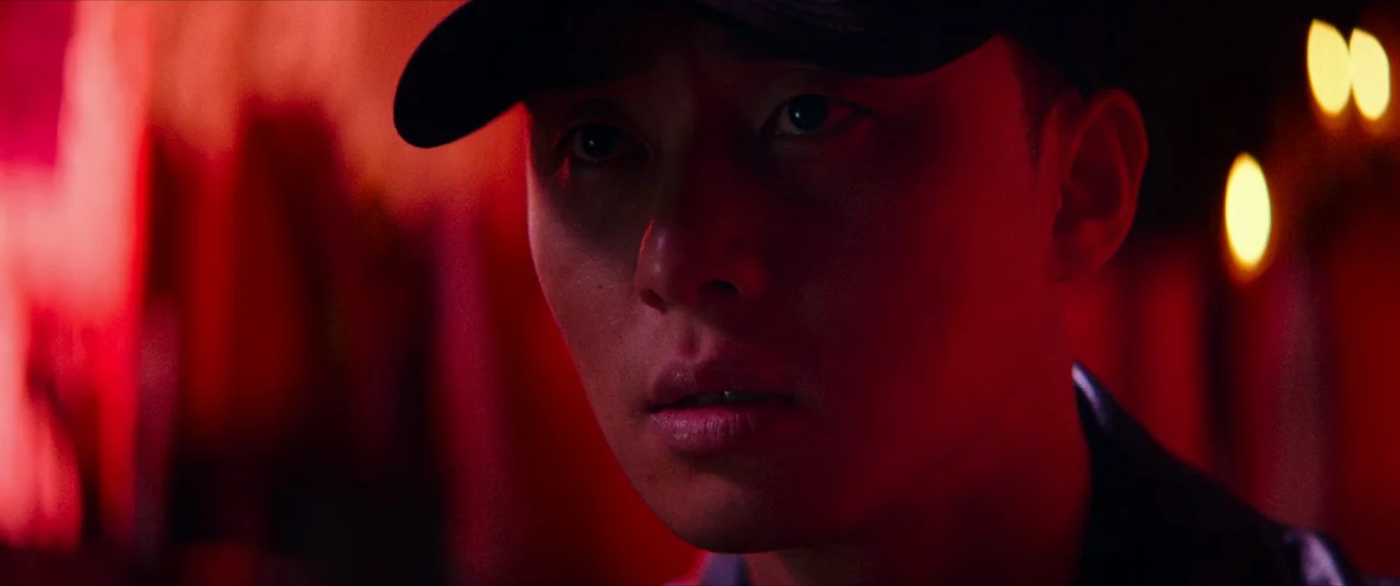 The Divine Fury (2019) movie still: closeup — A dimly lit space is saturated in intense red light. A young man wearing a cap stares forward.