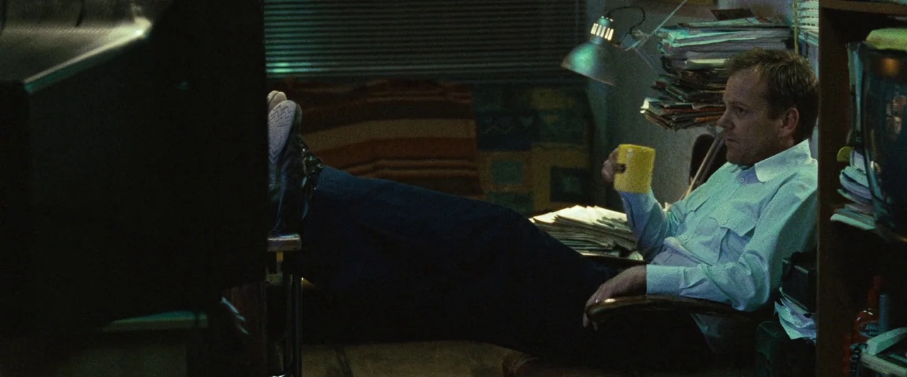 Mirrors (2008) movie still: medium — A cluttered office space is filled with stacks of papers and electronic equipment. A man sits in a chair with…