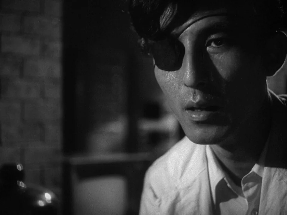 Godzilla (1954) (1954) movie still: closeup — A dimly lit room with exposed brick walls and medical equipment blurred in background. A man with a…