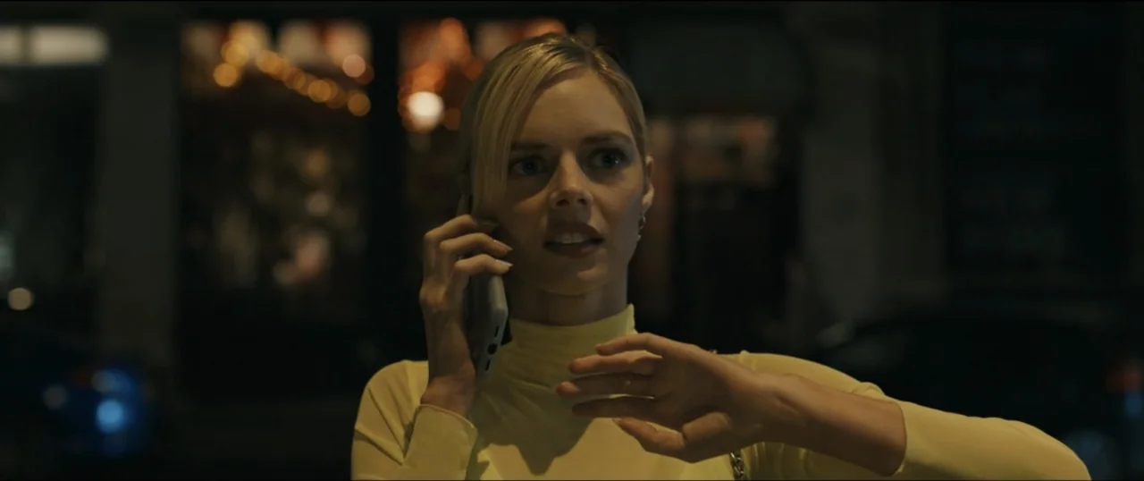 Scream VI (2023) movie still: medium — An outdoor city street at night with a blurred background showing dark urban textures. A blonde woman in a…