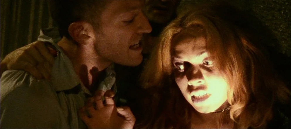 Irréversible (2002) movie still: closeup — A dark indoor space with minimal ambient light. A woman is illuminated from below as a man stands…