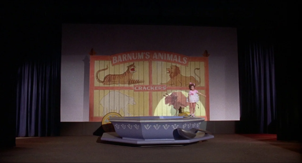What’s the Matter with Helen? (1971) movie still: wide — A dark, empty stage features a large projected backdrop of a Barnum's Animals box. A young…