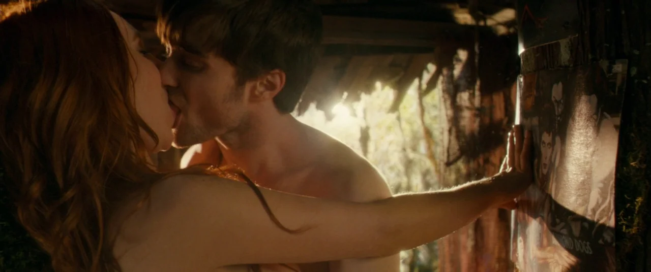 Horns (2013) movie still: closeup — A rustic wooden shelter has a David Bowie Diamond Dogs poster tacked to a beam. A shirtless man and a woman are…