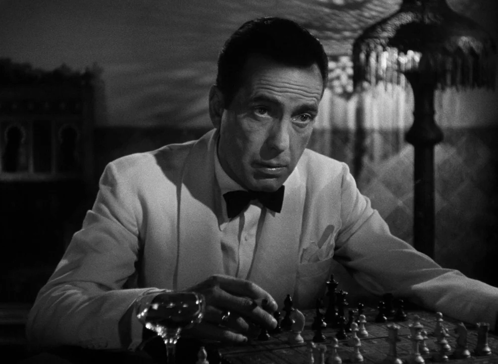 Casablanca (1942) movie still: medium — An interior space contains a chess set on a wooden surface. A man in a dinner jacket plays a game of chess…