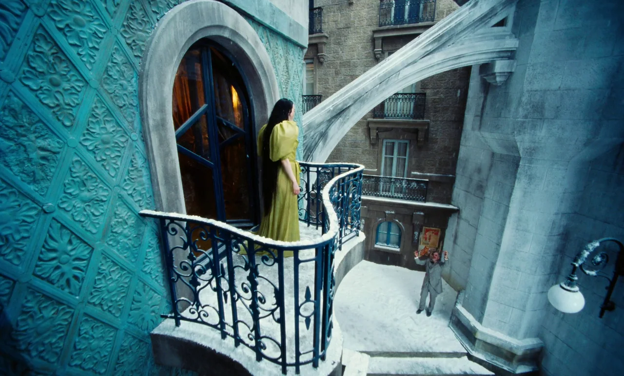 Poor Things (2023) movie still: wide — A surreal blue-tiled balcony overlooks a snow-covered courtyard in a stone building complex. A woman in a…