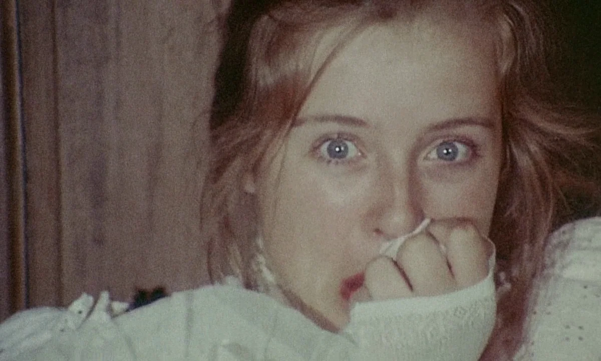 Immoral Tales (1974) movie still: closeup — A dimly lit indoor space with textured walls and a slightly grainy analog film look. A young woman with…