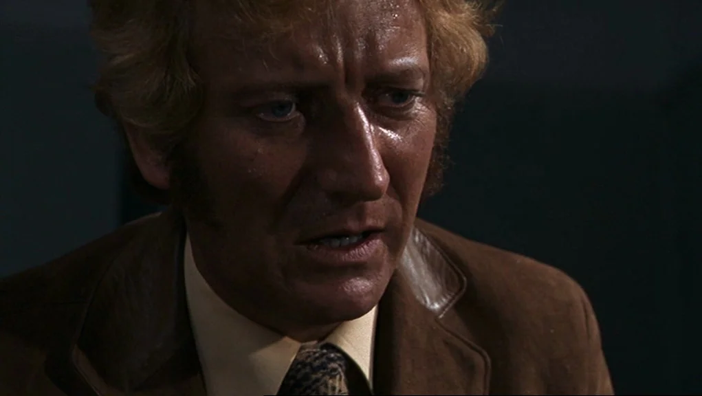 Frenzy (1972) movie still: closeup — A man stands in a dimly lit room against a dark, featureless backdrop. He looks slightly off-camera with a…