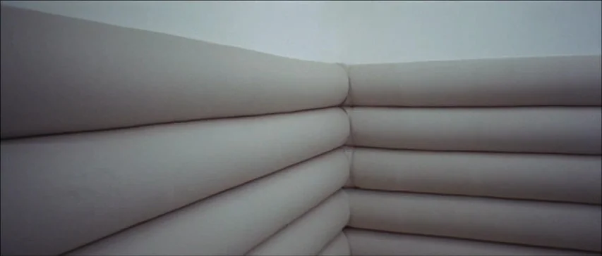 Four Flies On Grey Velvet (1971) movie still: establishing — A corner of a room features white horizontal padded walls. The surface consists of…