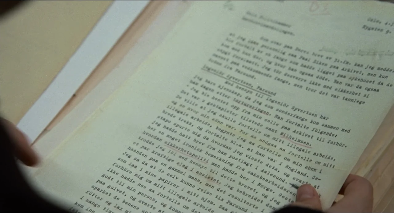 Sentimental Value (2025) movie still: closeup — An aged sheet of typed Norwegian documentation lies held within human hands. The paper exhibits a…
