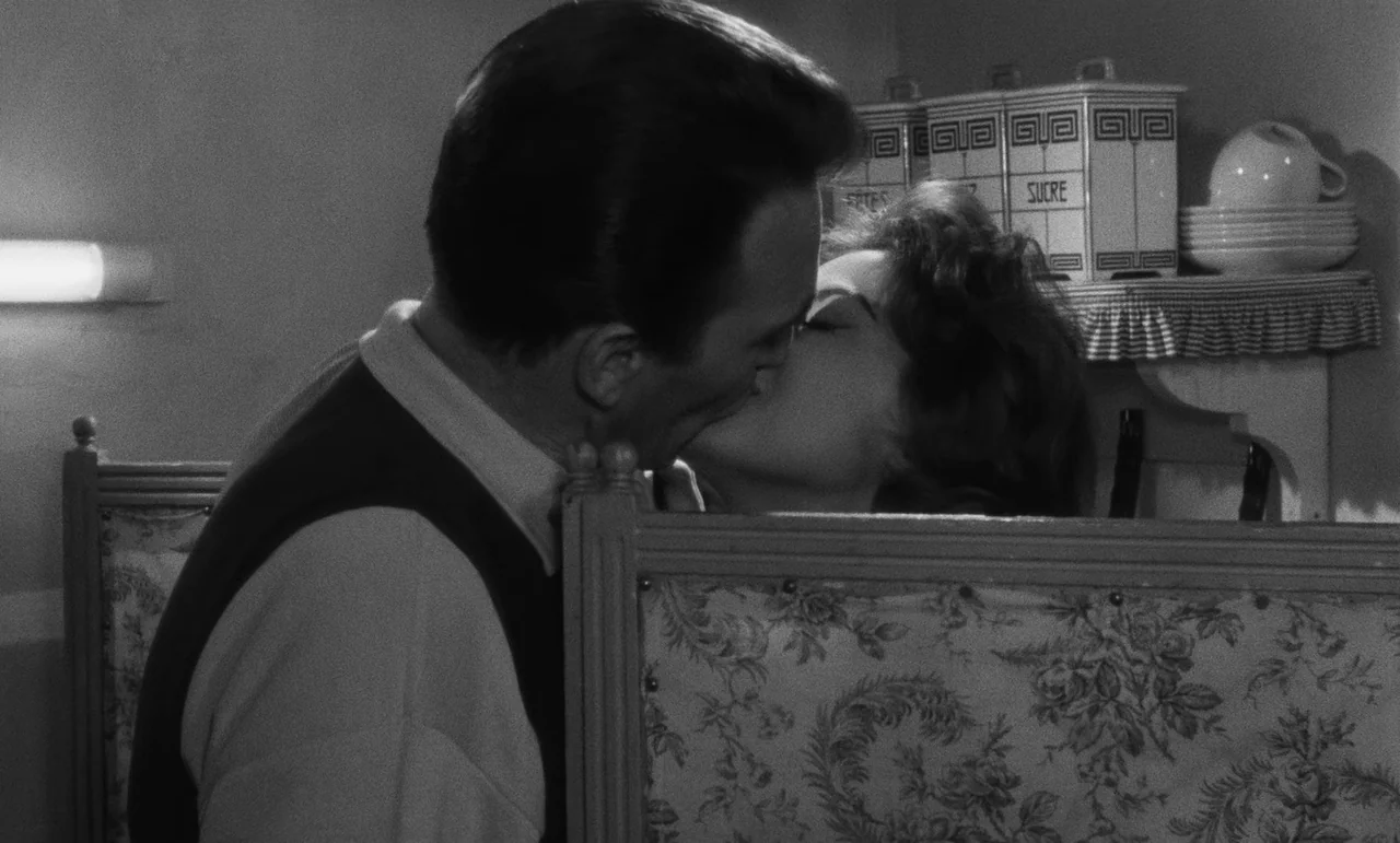 Witness In The City (1959) movie still: medium — A dark booth with floral fabric upholstery sits in a classic diner setting. A man and a woman share…