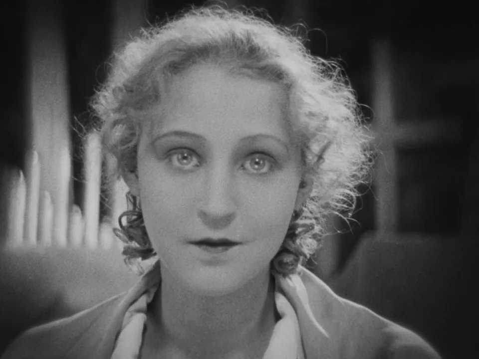 Metropolis (1927) movie still: closeup — A dimly lit space features blurred upright structures reminiscent of candles in the background. A woman…