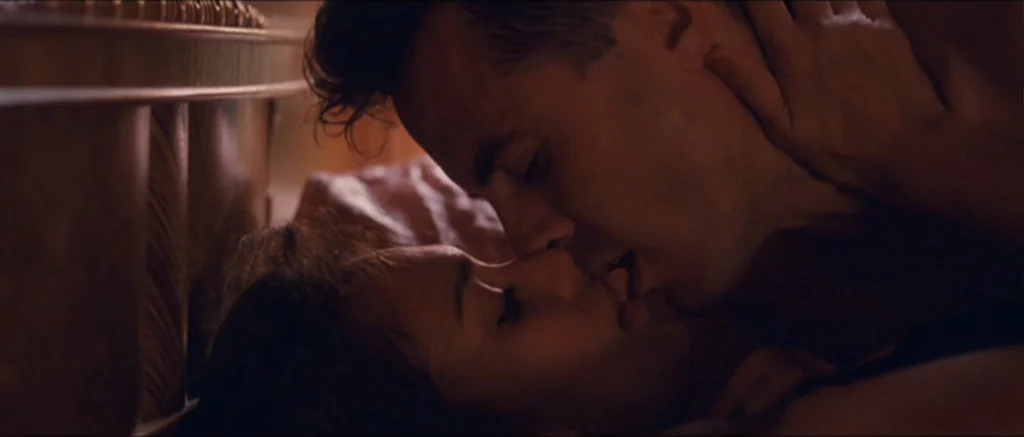 The Killer Inside Me (2010) movie still: closeup — Two individuals lie in a dimly lit bedroom against a wooden headboard. The couple engages in a…