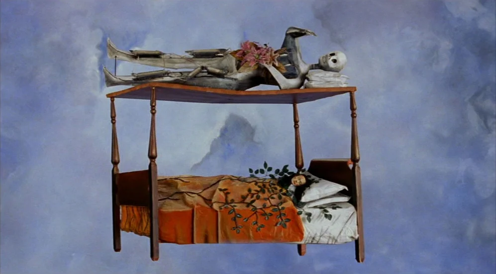 Frida (2002) movie still: wide — A canopy bed floats in a blue sky painted with stylized clouds. A human skeleton rests on the wooden top of the…