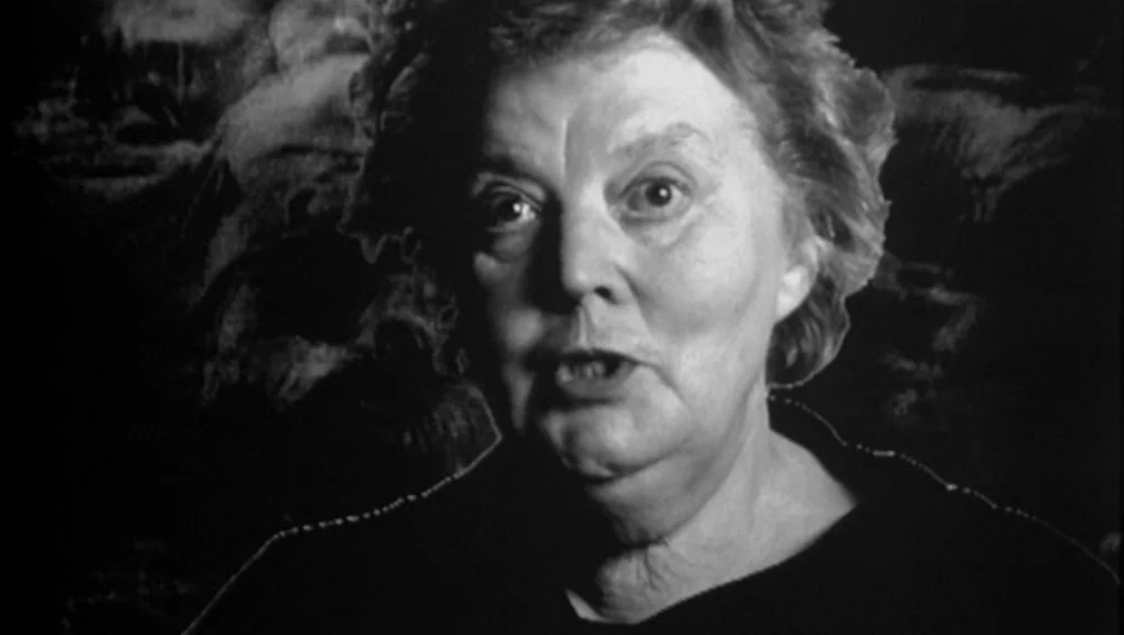 War Requiem (1989) movie still: closeup — An interior space with a dark, textured background behind the subject. A woman faces the camera directly…