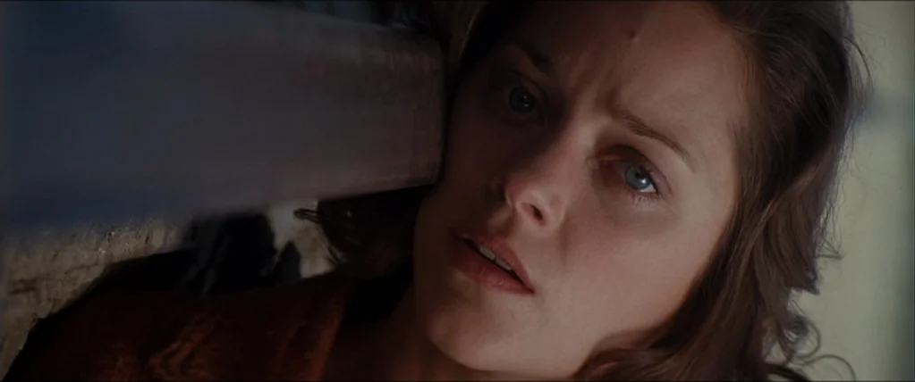Inception (2010) movie still: closeup — A close up portrait shows a woman pressing her face against a beam. She looks forward with a steady gaze…