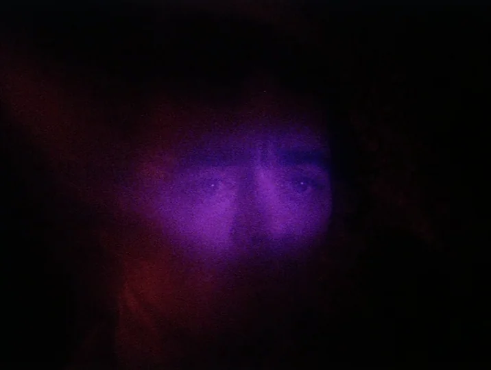 Careful (1992) movie still: closeup — A dark, underexposed environment leaves most of the frame in total shadow. A man's face emerges from the…