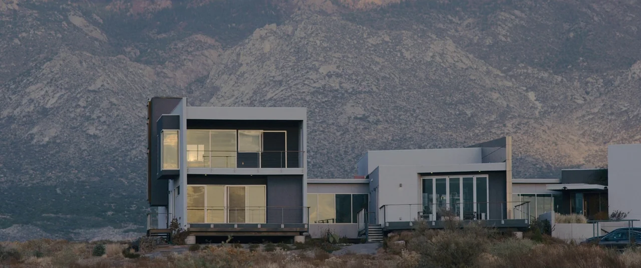 Intrusion (2021) movie still: establishing — A modern multi-level house with glass walls sits at the base of large mountains. The structure features…