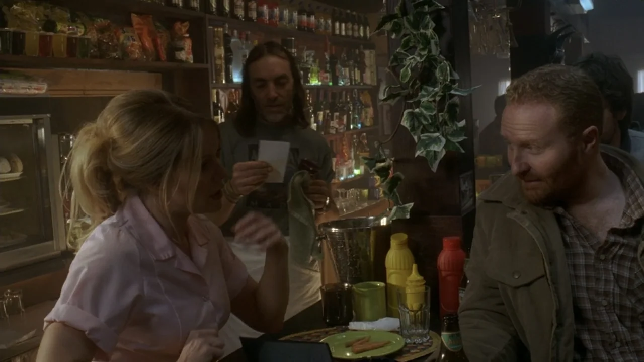 The Shepherd (2023) movie still: medium — A diner counter with a bartender serving a man and a woman. The three individuals converse while standing…