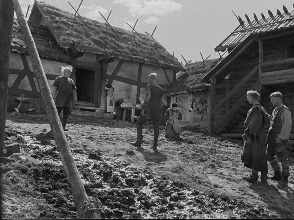 The Virgin Spring (1960) movie still: wide — A cluster of thatched-roof timber structures sit around a muddy communal yard. Several figures in…