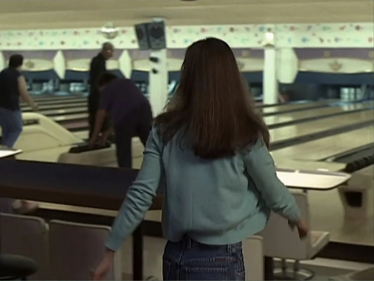 Catch a Falling Star (2000) movie still: medium — An indoor recreation center features polished wooden lanes and a lounge seating area. A woman in a…