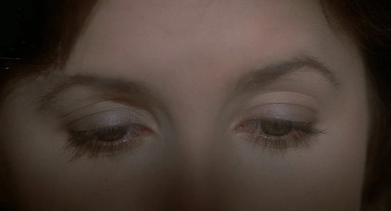 Inferno (1980) movie still: closeup — A close view shows the upper portion of a woman's face in shadow. The subject keeps her eyes closed.