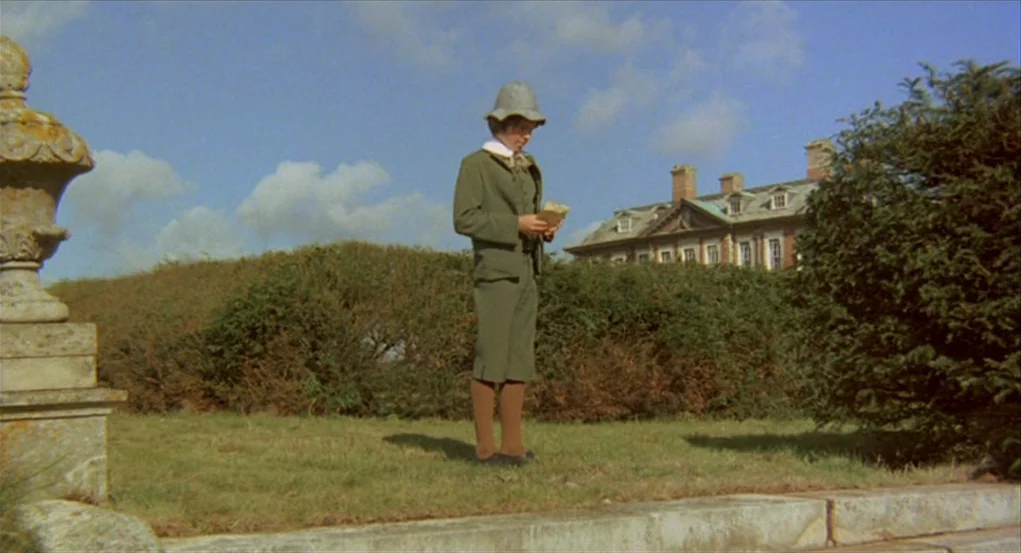 The Go-Between (1971) movie still: fullbody — A well-manicured manor lawn features a stone ornament and a large house in back. A young boy wearing…