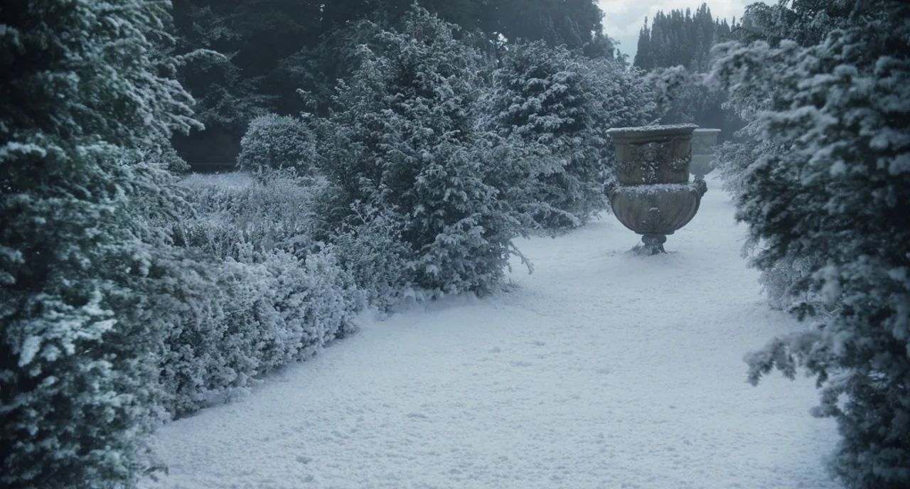 The Little Stranger (2018) movie still: wide — A snow-covered formal garden features neatly trimmed hedges and stone urns. The ground is buried…
