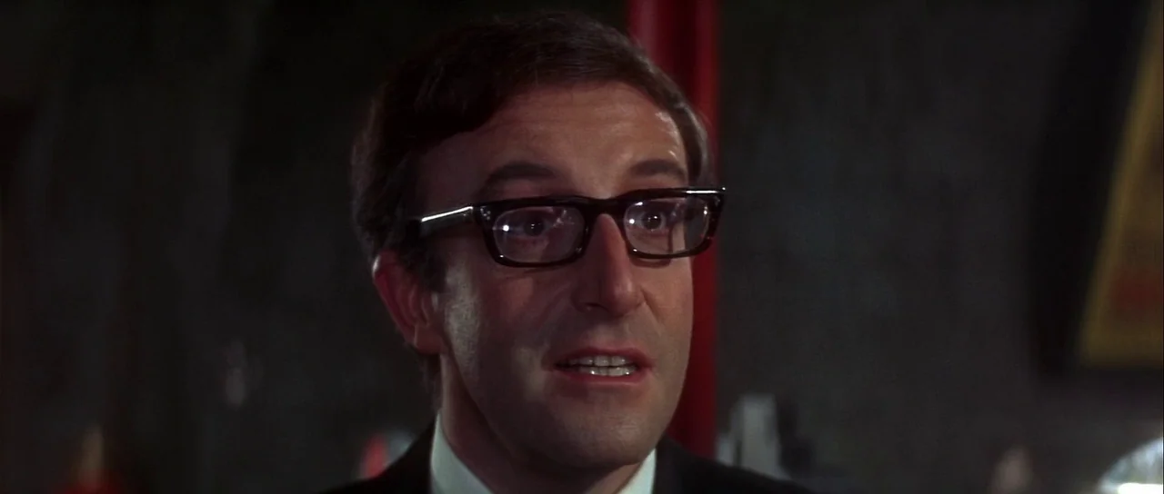 Casino Royale (1967) (1967) movie still: closeup — A man stands in a dimly lit laboratory with dark, textured walls behind him. He wears heavy…