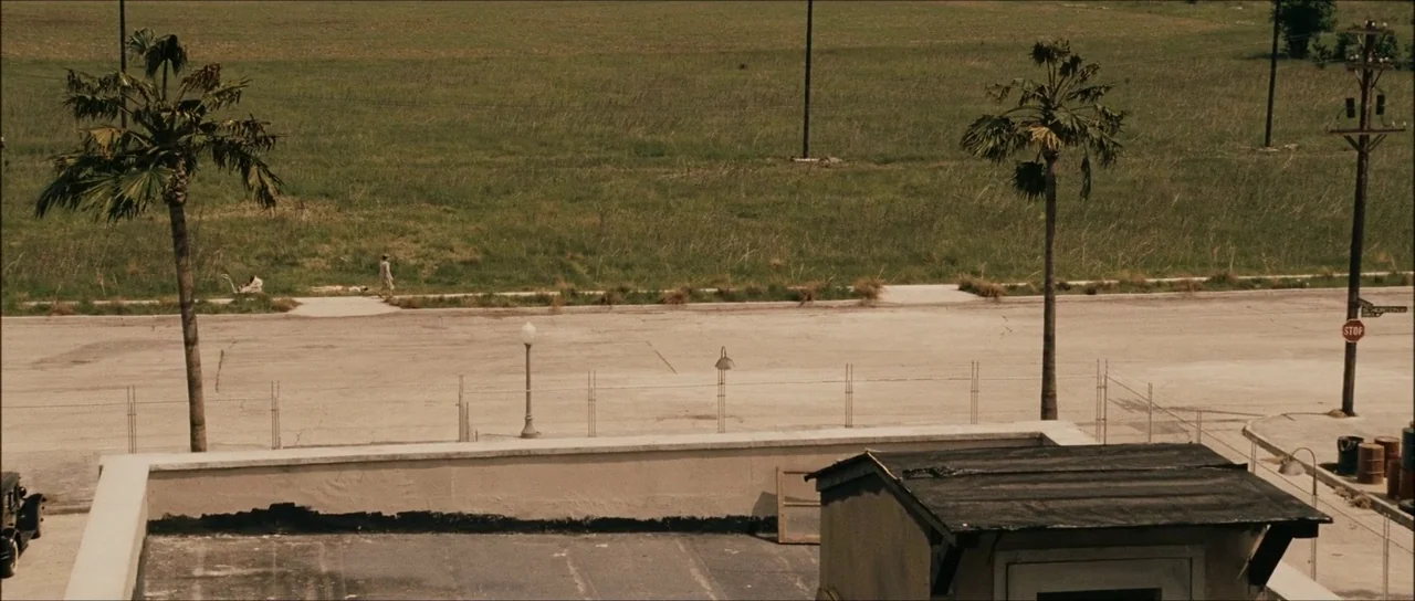 The Black Dahlia (2006) movie still: wide — A dusty urban lot sits before a large, dry expanse of undeveloped field. A single person walks along the…