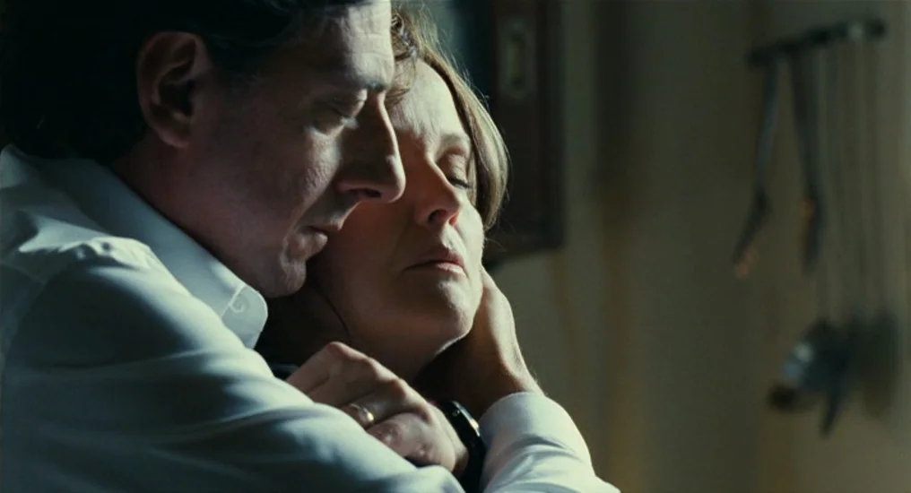 Paris, Je T’Aime (2006) movie still: closeup — A dimly lit domestic interior features blurred kitchen utensils on a wall rack. A man leans in…