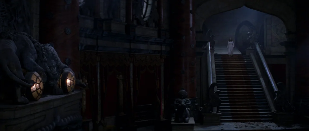 The Haunting (1999) movie still: wide — A dark, expansive stone hall features ornate carvings and statues of lions and griffins. A woman in a white…