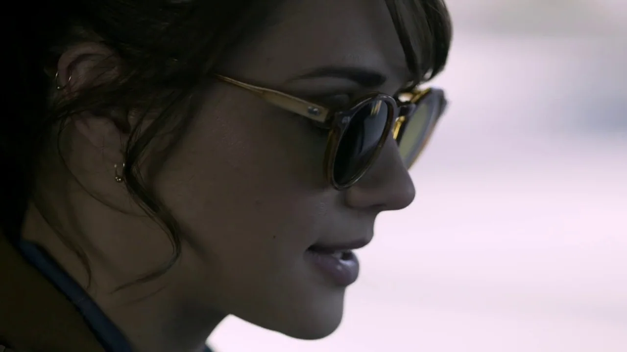 Hellraiser: Judgement (2018) movie still: closeup — A close-up shot of a young woman's profile while sitting inside a vehicle. She wears sunglasses…