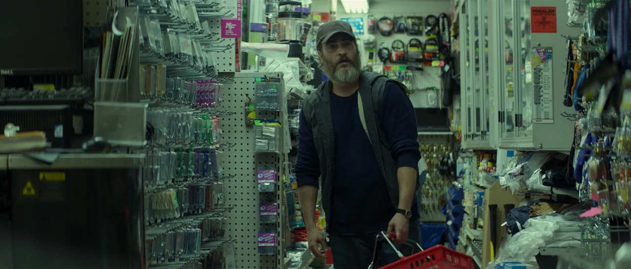 You Were Never Really Here (2017) movie still: medium — A cramped hardware store aisle is packed with merchandise on both sides on pegboards. A man…