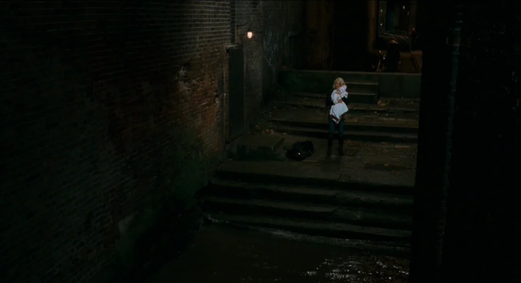 Eastern Promises (2007) movie still: wide — A dark urban alleyway features high brick walls and a small set of stairs. A woman stands alone on the…