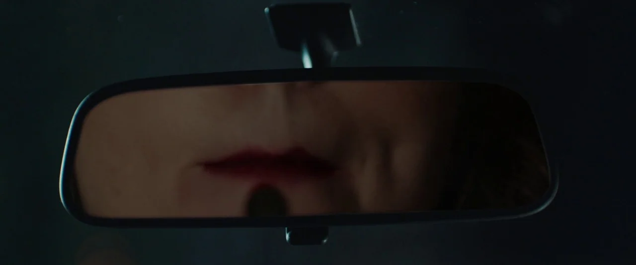Extra Ordinary (2019) movie still: closeup — A close-up view through a vehicle rearview mirror focuses on a mouth. The lips are painted dark red and…